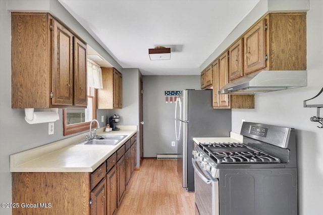 kitchen featuring a sink, light countertops, light wood finished floors, under cabinet range hood, and stainless steel appliances