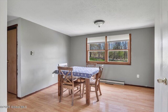 dining room with a textured ceiling, baseboards, a baseboard heating unit, and light wood-style flooring