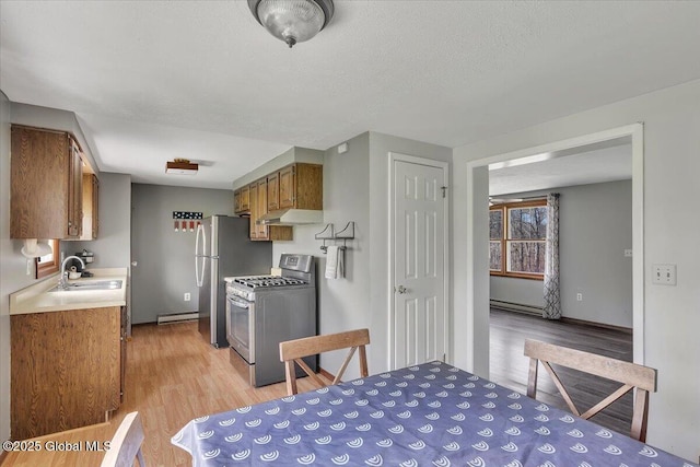 kitchen with light wood-type flooring, a baseboard heating unit, under cabinet range hood, a sink, and stainless steel appliances
