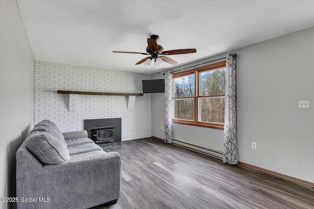 living area with a wood stove, wood finished floors, ceiling fan, baseboard heating, and a textured ceiling