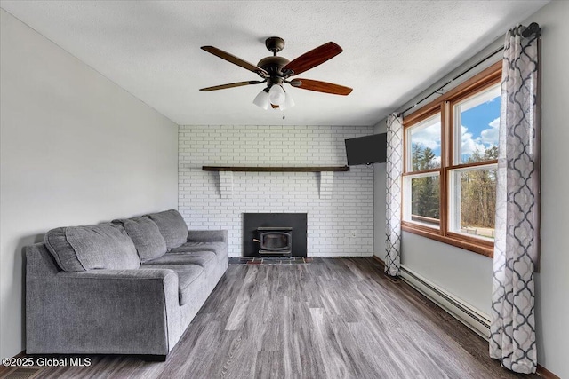 living room featuring ceiling fan, wood finished floors, a wood stove, and a baseboard radiator