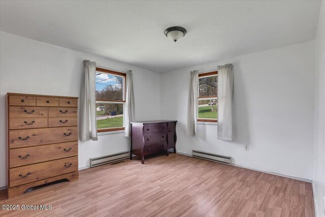 bedroom with a baseboard heating unit and light wood-style floors
