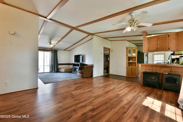 unfurnished living room with lofted ceiling with beams, a wood stove, a ceiling fan, wood finished floors, and wallpapered walls
