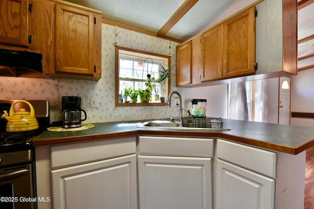 kitchen with a sink, stainless steel range with gas stovetop, wallpapered walls, and dark countertops