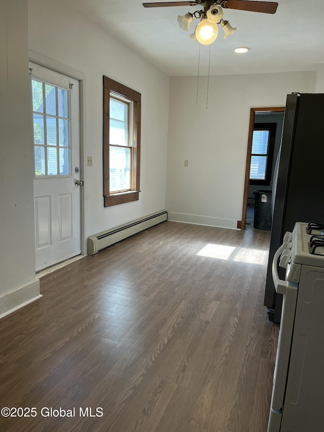 unfurnished dining area with baseboard heating, a ceiling fan, dark wood-style floors, and a wealth of natural light