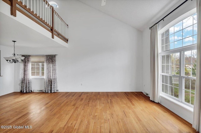 empty room featuring an inviting chandelier, visible vents, wood finished floors, and a wealth of natural light