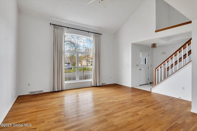 unfurnished living room featuring a textured ceiling, visible vents, wood finished floors, high vaulted ceiling, and stairs