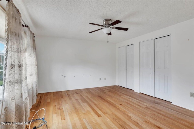 unfurnished bedroom featuring wood finished floors, a textured ceiling, ceiling fan, and two closets