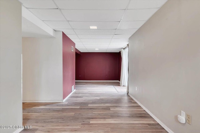 corridor with baseboards, wood finished floors, and a paneled ceiling