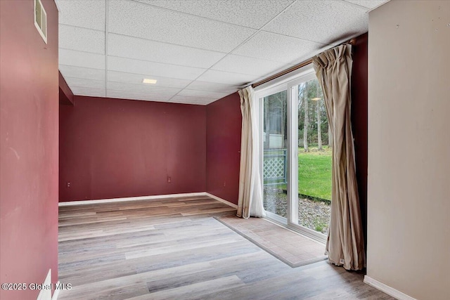 unfurnished room with baseboards, visible vents, a drop ceiling, and wood finished floors
