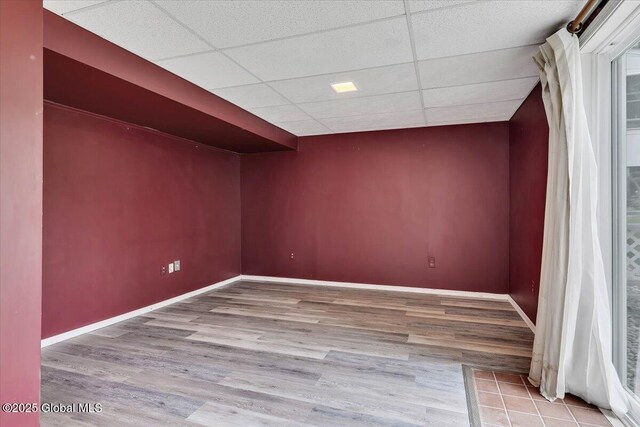 interior space with baseboards, a drop ceiling, and wood finished floors