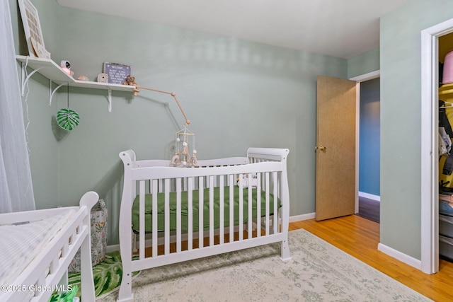 bedroom with baseboards, a crib, and wood finished floors