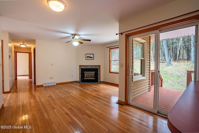 unfurnished living room with light wood-type flooring, ceiling fan, a tile fireplace, baseboards, and visible vents