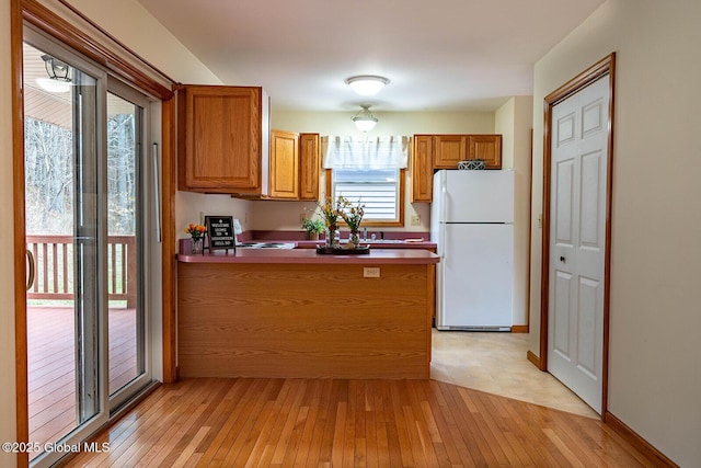 kitchen featuring brown cabinets, a peninsula, light wood-style flooring, and freestanding refrigerator