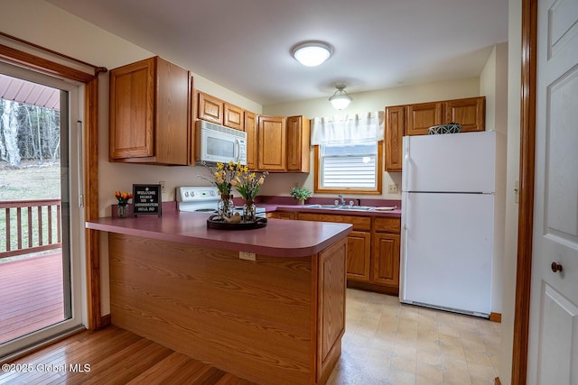kitchen featuring brown cabinetry, a peninsula, dark countertops, and white appliances