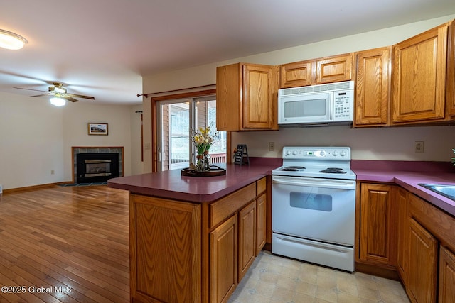 kitchen featuring brown cabinetry, a peninsula, white appliances, and dark countertops