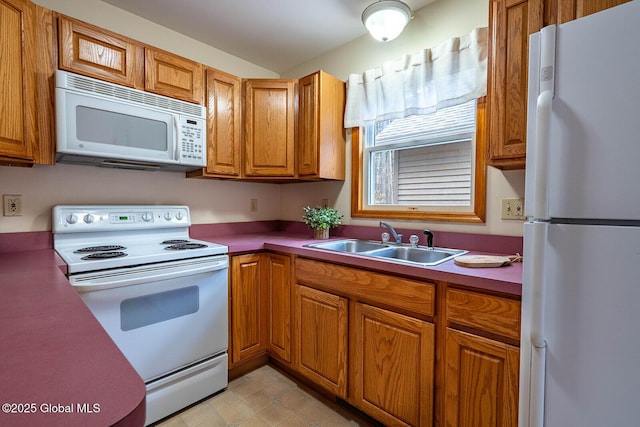 kitchen with brown cabinetry, a sink, and white appliances