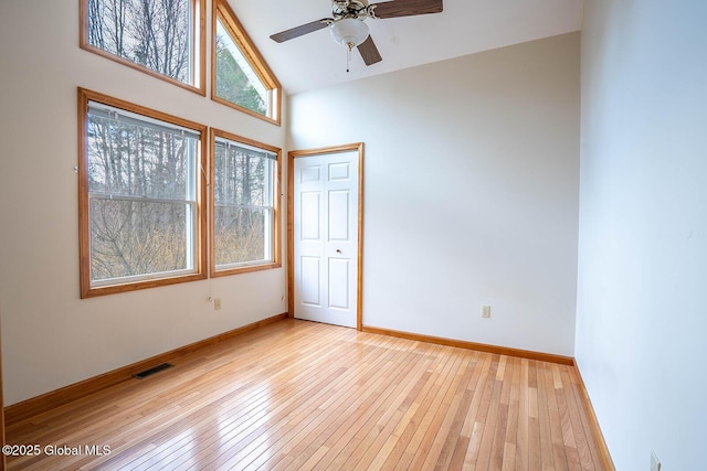 unfurnished room featuring baseboards, visible vents, light wood-style floors, a ceiling fan, and high vaulted ceiling