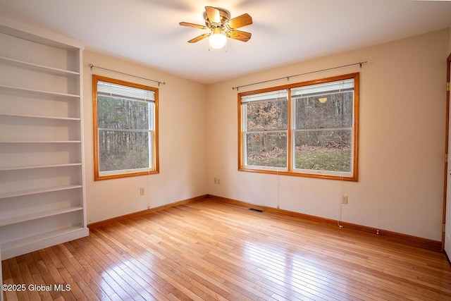 spare room with light wood-style flooring, visible vents, a ceiling fan, and baseboards