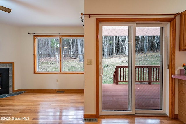 doorway with light wood finished floors, a tile fireplace, visible vents, and a wealth of natural light
