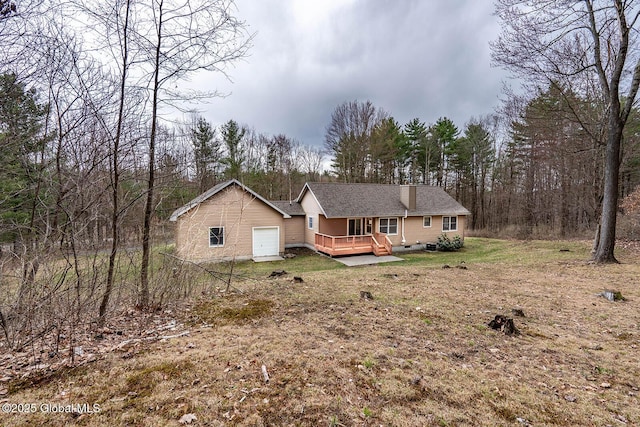 back of property with a forest view, a lawn, a chimney, a deck, and a garage
