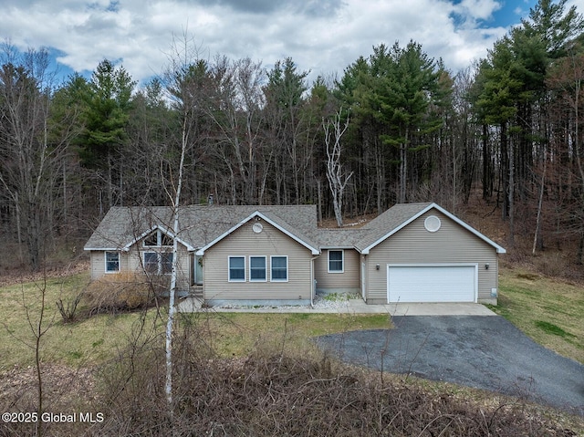 single story home featuring a forest view, a front lawn, driveway, a shingled roof, and an attached garage