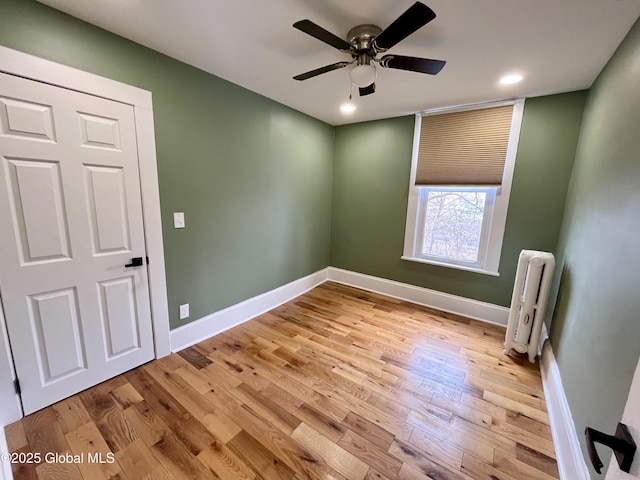 empty room featuring wood finished floors, ceiling fan, baseboards, and radiator heating unit