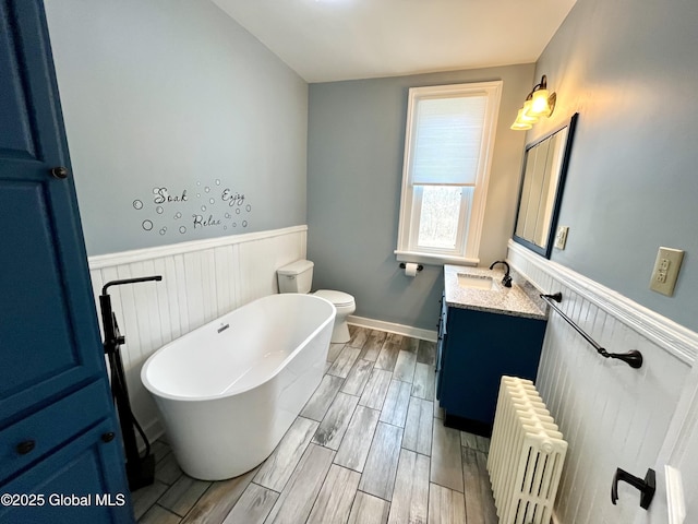 bathroom with radiator heating unit, vanity, a wainscoted wall, wood finished floors, and a freestanding bath