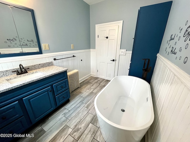 full bath featuring a freestanding tub, radiator, vanity, wood finished floors, and a wainscoted wall