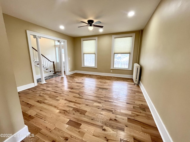 unfurnished living room featuring a wealth of natural light, a ceiling fan, radiator, and wood finished floors