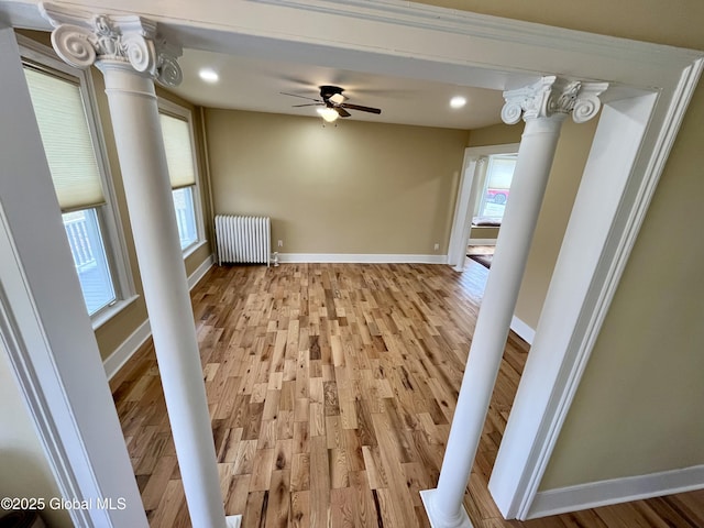 unfurnished living room featuring baseboards, recessed lighting, radiator heating unit, ornate columns, and light wood-style flooring
