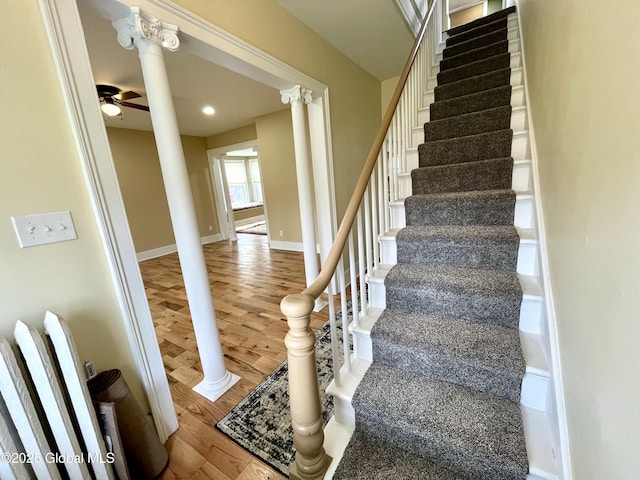 staircase with decorative columns, ceiling fan, baseboards, and wood finished floors