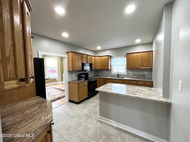 kitchen featuring a sink, a peninsula, brown cabinetry, black appliances, and light stone countertops
