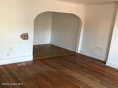 empty room with arched walkways, baseboards, and wood-type flooring