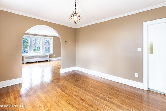 spare room with radiator, arched walkways, crown molding, baseboards, and light wood-style floors