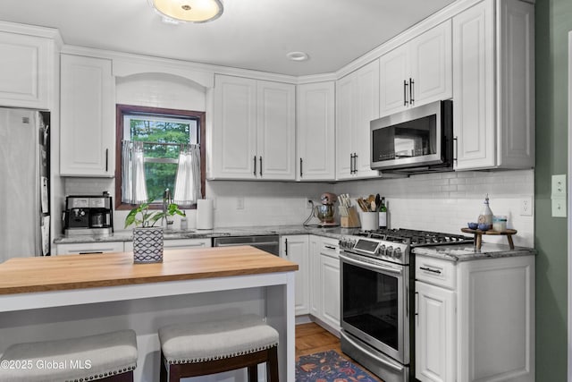 kitchen with decorative backsplash, a kitchen bar, wood counters, stainless steel appliances, and white cabinetry