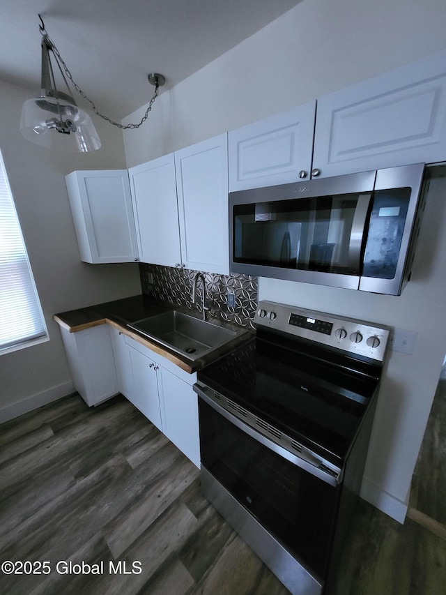 kitchen with white cabinets, dark countertops, a sink, stainless steel appliances, and decorative backsplash