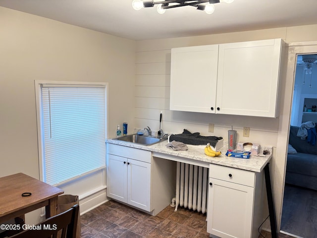 kitchen featuring a sink, light countertops, radiator heating unit, and white cabinetry