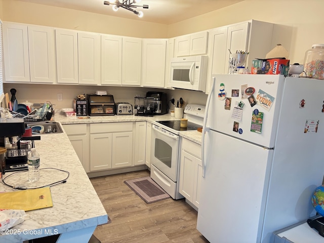 kitchen with white cabinets, white appliances, light countertops, and light wood finished floors