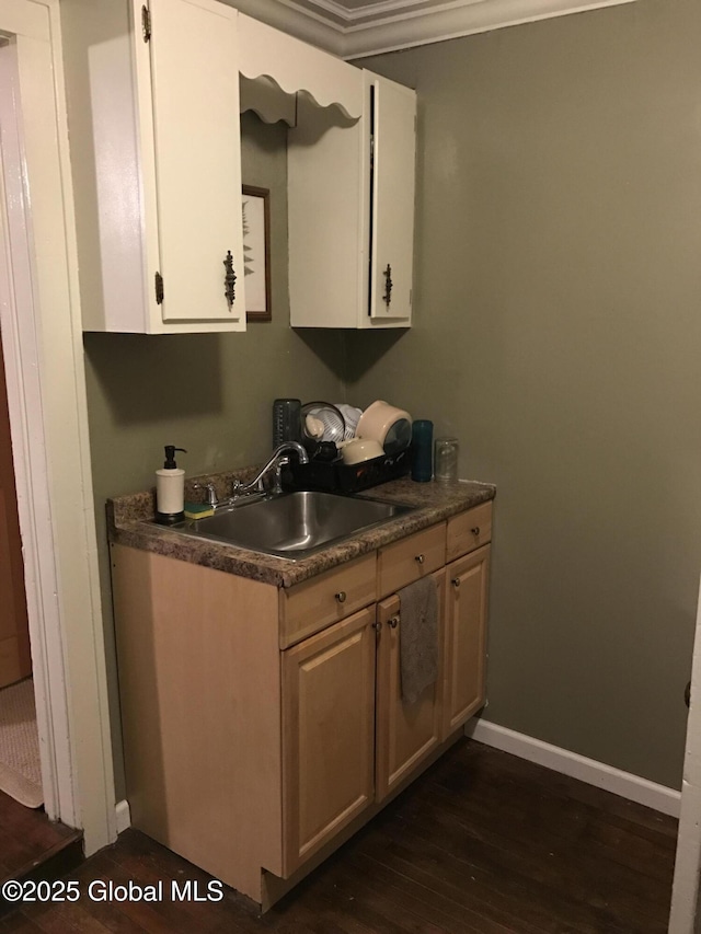 kitchen featuring white cabinets, dark wood-style floors, a sink, dark countertops, and baseboards