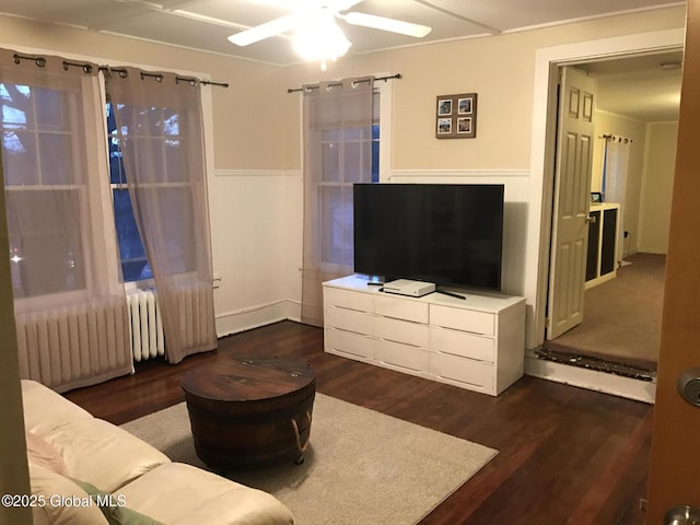 living area with wainscoting, a ceiling fan, radiator heating unit, and dark wood-style floors