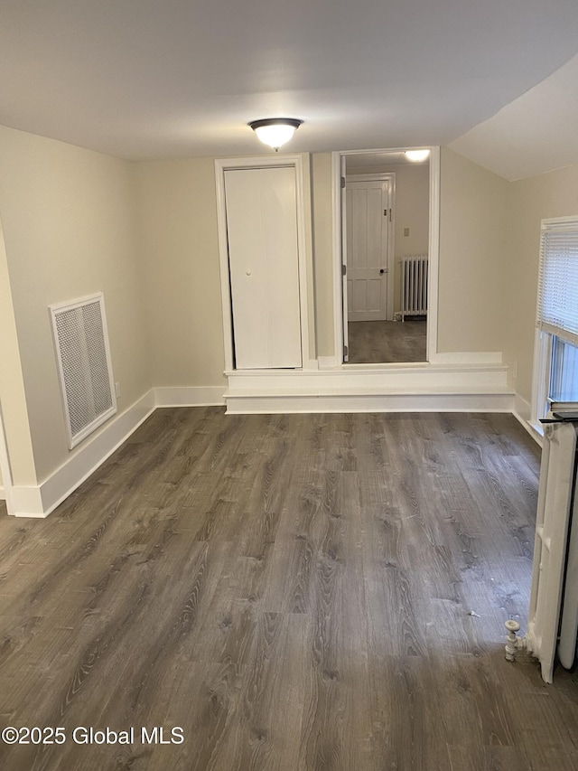 spare room featuring radiator heating unit, baseboards, lofted ceiling, dark wood-style flooring, and visible vents