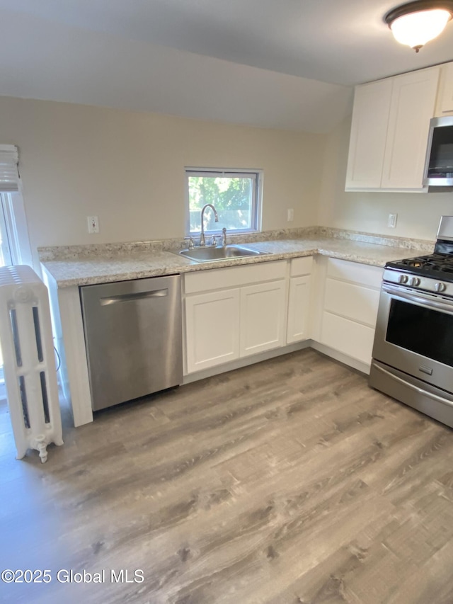 kitchen with white cabinetry, a sink, light wood-style floors, and appliances with stainless steel finishes