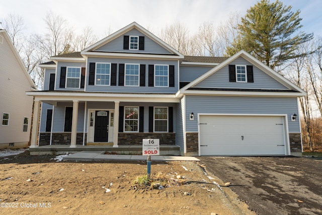 view of front of house with aphalt driveway, stone siding, an attached garage, and covered porch