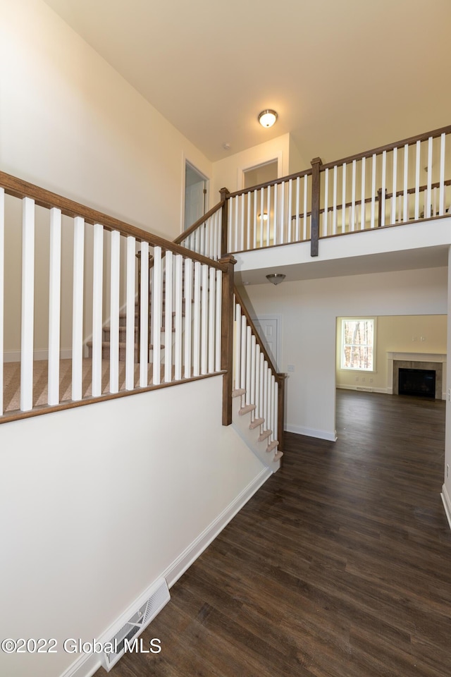 stairs featuring baseboards, a high ceiling, wood finished floors, and a fireplace