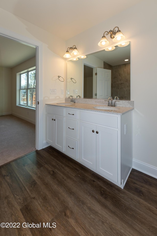 full bath featuring wood finished floors, double vanity, a sink, and baseboards