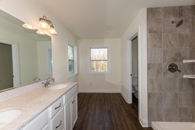 bathroom featuring a tile shower, a sink, toilet, and wood finished floors