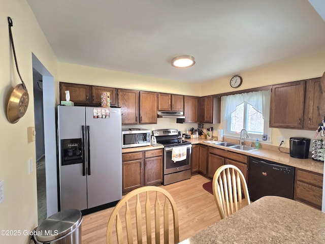 kitchen featuring a sink, light wood-style floors, light countertops, under cabinet range hood, and appliances with stainless steel finishes