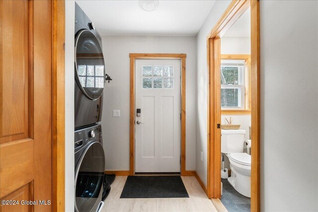 washroom with light wood finished floors, stacked washing maching and dryer, laundry area, and baseboards