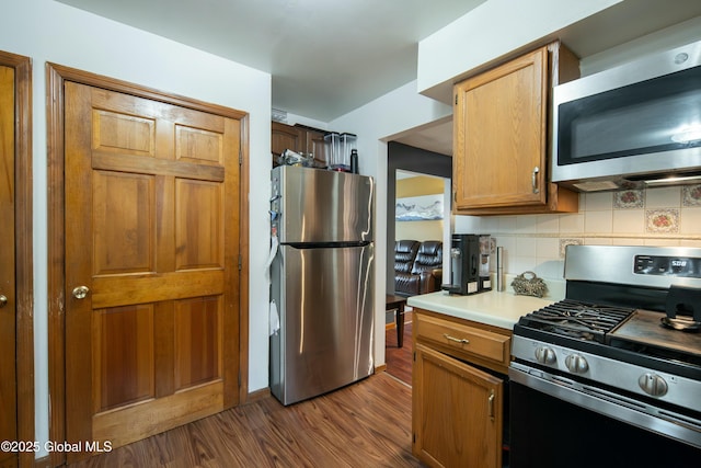 kitchen with stainless steel appliances, tasteful backsplash, light countertops, and dark wood finished floors
